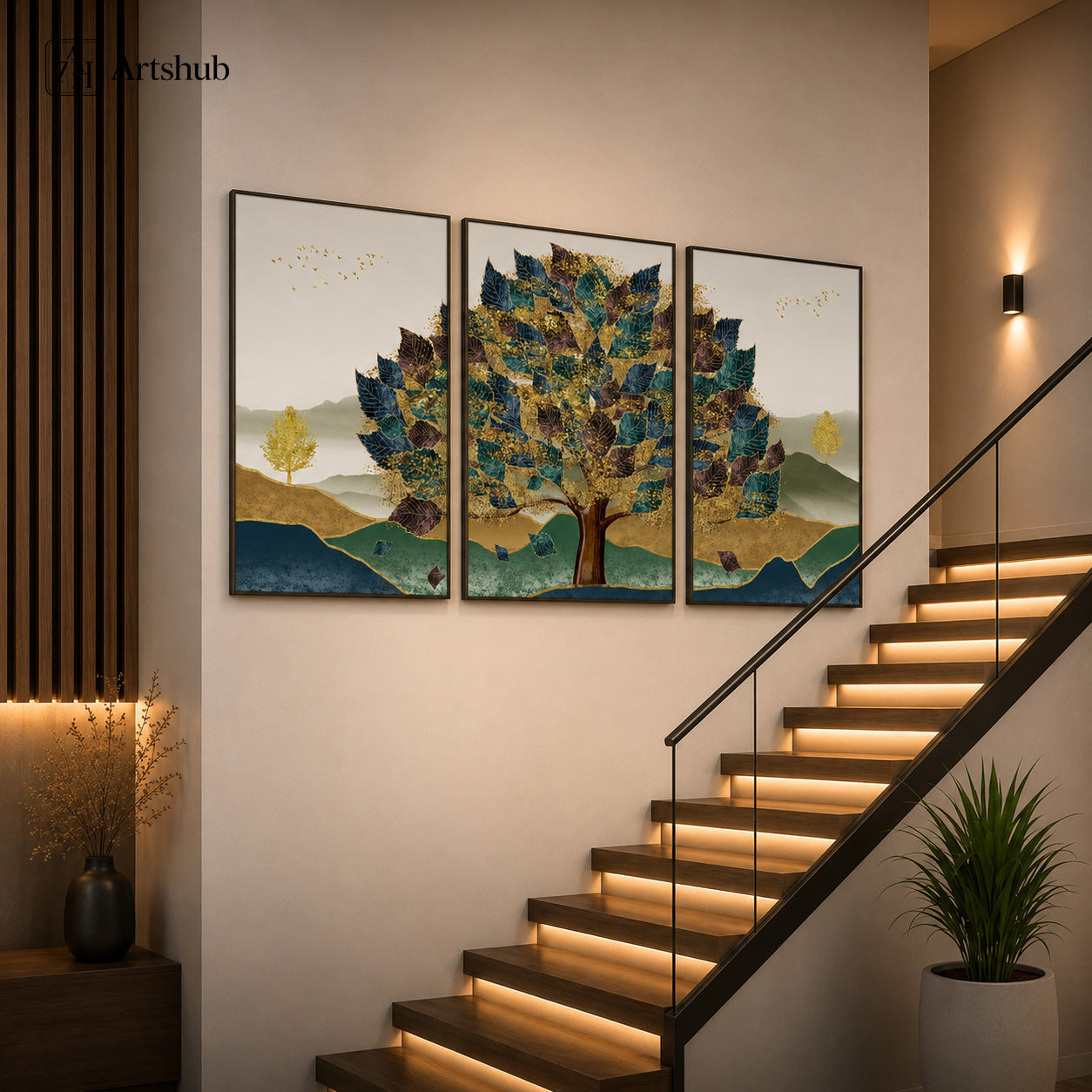 Artshub Golden Canopy 3-panel triptych canvas framed wall art displayed on a warm beige staircase wall with LED-lit wooden stairs, black vase with dried branches and green plant – majestic tree with teal, navy, gold and dark brown leaves, golden branches, birds in flight, misty mountain landscape in sage green and gold, deep teal river, warm golden earth, black floater frame