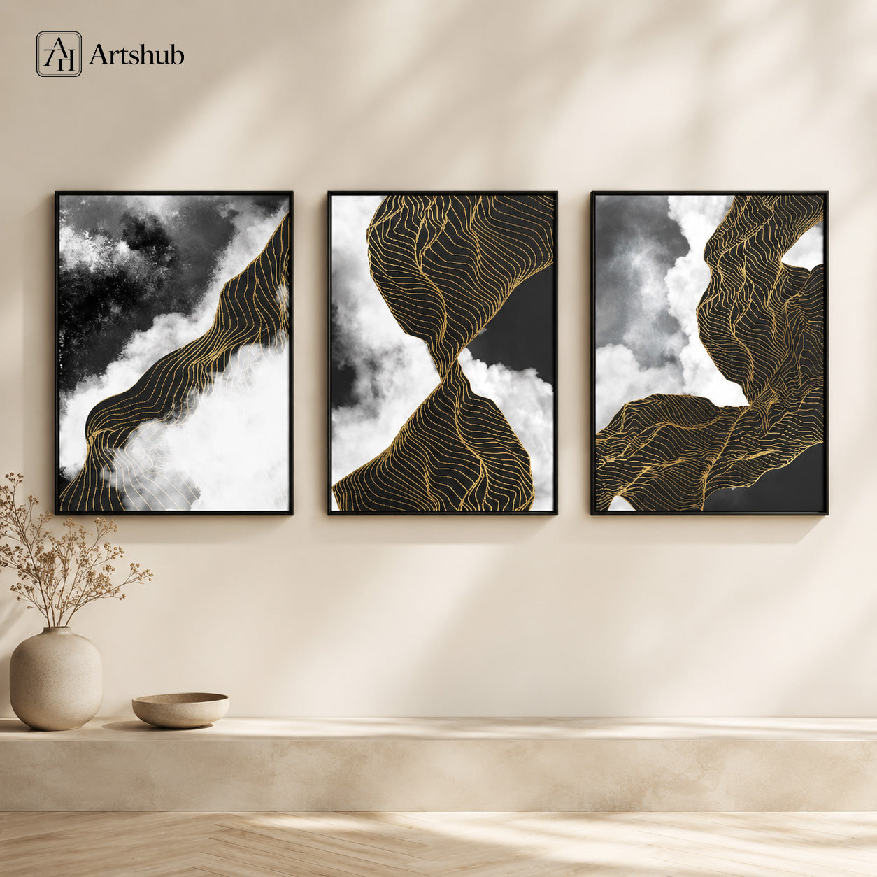 Artshub Obsidian Flow 3-panel triptych abstract canvas framed wall art displayed on a warm cream wall with large round ceramic vase with dried flowers and small ceramic bowl – bold abstract black and white cloud formations with flowing golden contour lines across three panels in premium black floater frames
